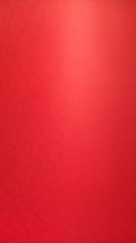 Beautiful red bright background. Color gradient depending on the lighting. Scarlet uneven color. A sheet of colored paper with natural light. Fragment of a sheet of colored paper with a glare of light