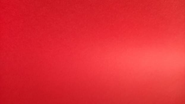 Beautiful red bright background. Color gradient depending on the lighting. Scarlet uneven color. A sheet of colored paper with natural light.Fragment of a sheet of colored paper with a glare of light.