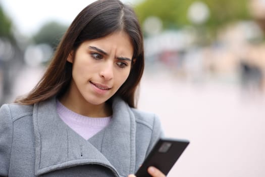 Angry woman checks phone in winter in the street