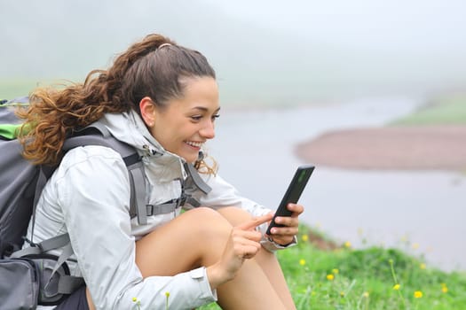 Happy hiker using smart phone sitting in nature in a riverside