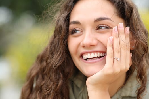 Happy fiencee smiling showing ring at camera in a park