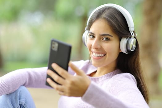 Happy woman listening to music looking at camera in a park