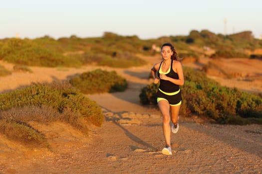 Front vie wof a runner woman running in the mountain towards camera at sunset