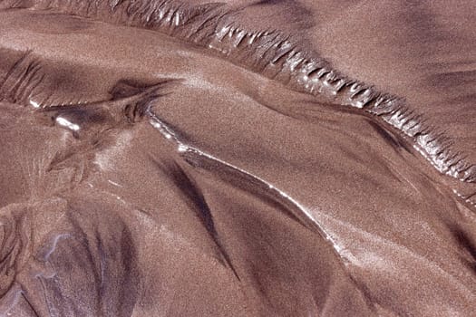 abstraktes Muster im dunklen Sand am Strand