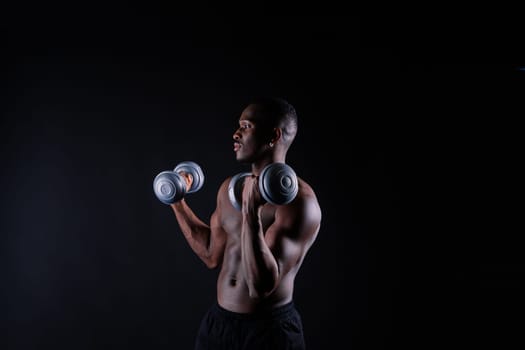 Isolated african muscular man with dumbbells on a dark studio background. Strong shirtless black guy