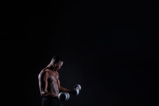 Isolated african muscular man with dumbbells on a dark studio background. Strong shirtless black guy