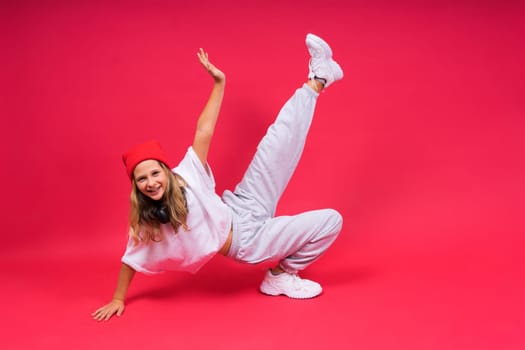 Girl listening to music in headphones on a red background. Cute child enjoying dance music, smile