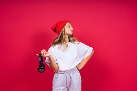 Girl listening to music in headphones on a red background. Cute child enjoying dance music, smile