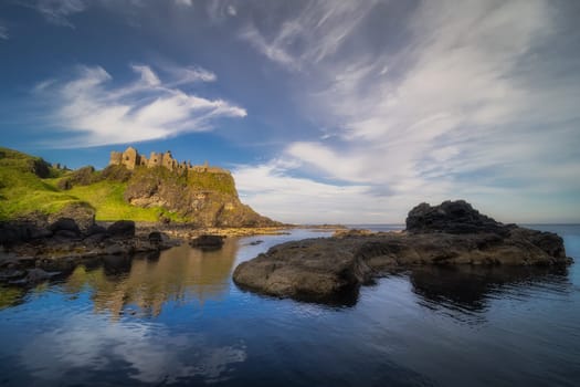 Dunluce Castle reflected in ocean, nested on the edge of cliff, part of Wild Atlantic Way, Northern Ireland. Filming location of popular TV show