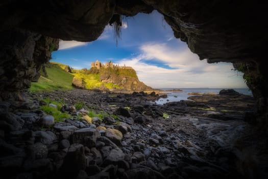 Dunluce Castle seen from a small cave on a shoreline, nested on the edge of cliff, part of Wild Atlantic Way, Bushmills, Northern Ireland