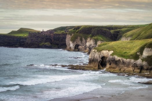 Dunluce Castle on the edge of cliff and limestone rock formations on White Rocks Beach, Causeway Coast, Wild Atlantic Way, Antrim, Northern Ireland