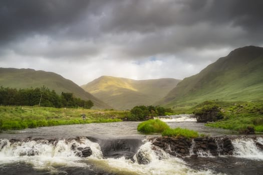 Mayo, Ireland, July 2020 Fisherman fishing on Bundoragha River with small waterfalls and cascades, Glenummera and Glencullin mountains in background