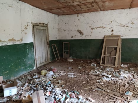 Serbia, Belgrade, May 10, 2020. Inside abandoned house. Grunge scene. Scattered trash on the floor. Green paint on the walls. White half wall. Shot wooden window frames. Bottles, pieces of paper.