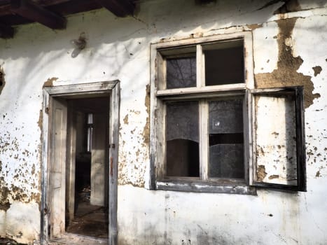 Old house with windows and a door. Collapsing rural house. The concept of urbanization and oblivion of the motherland. Abandoned house. Broken glass in the window and falling plaster. Serbia. Balkans.