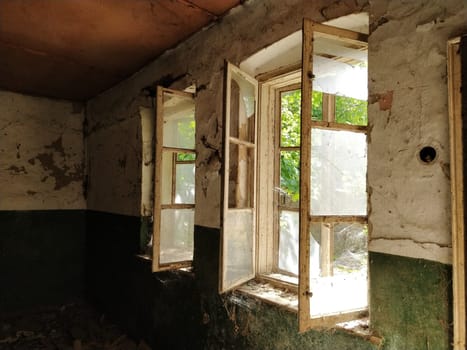 Inside abandoned house. View on broken window with curtain. Grunge scene. Through the old wooden frames with broken glass breaks warm sunlight. Sentimental sadness over bygone times. The concept of change, generational change, abandonment, uselessness.
