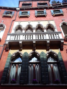 Venice, Italy. May 30, 2020. Facade of a beautiful Venetian building. The palace has pink walls, many windows and wooden shutters. View from below. A masterpiece of Venetian architecture. Journey to Italy