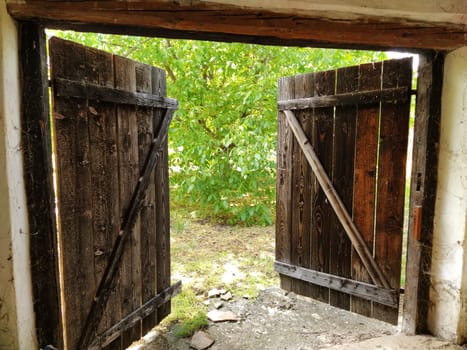 Beautiful old wooden open door. Inside view of the room. Crib doors, stall for livestock or garage. Wooden beams and doorway. Summer greens from the door. Doorway to the unknown.
