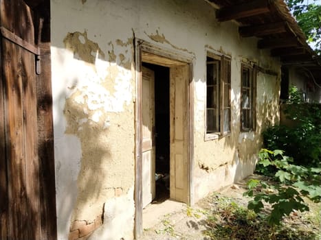 Wall with old windows and a door in a collapsing rural house. The concept of urbanization and oblivion of the motherland. Abandoned house. Broken glass in the windows, open door, falling plaster.