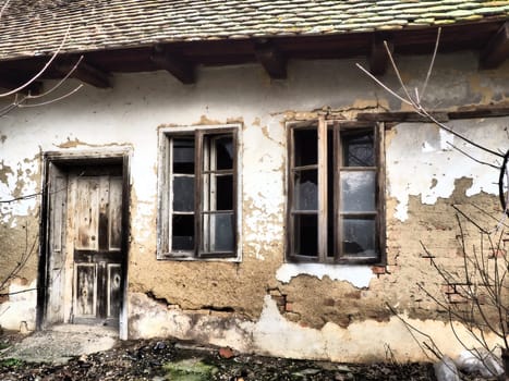 Old house with windows and a door. Collapsing rural house. The concept of urbanization and oblivion of the motherland. Abandoned house. Broken glass in the window and falling plaster. Serbia. Balkans.