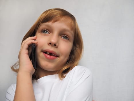 7-year-old girl with no front tooth. The child smiles, looks away and talks on the phone or smartphone. Change of milk teeth in childhood. Orthodontics and dental practice.