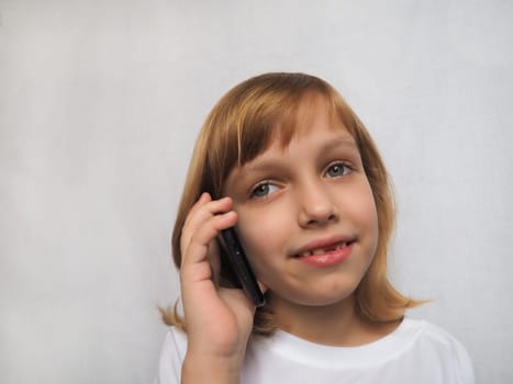 7-year-old girl with no front tooth. The child smiles, looks away and listens to someone on the phone or smartphone. Change of milk teeth in childhood. Modern communication technologies.