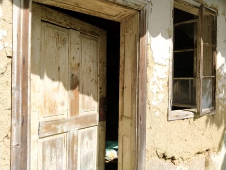 Wall with old windows and a door in a collapsing rural house. The concept of urbanization and oblivion of the motherland. Abandoned house. Broken glass in the windows, open door, falling plaster.