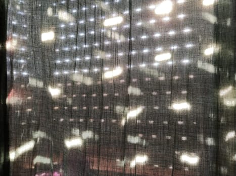 Sunlight shines through blinds with small holes and gray curtains - tulle. Abstract image. Summer mood. Reflection of light spots on fabric
