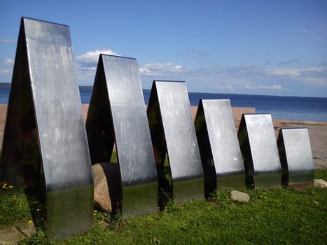 Metal steel structures shining in the sun. In the background is a lake and sky, in the foreground is green grass