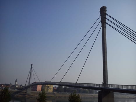 Bridge over the Sava river in the town of Sremska Mitrovica, Serbia. New concrete footbridge with metal cables. Engineering construction technologies. On the opposite bank is an old European city.