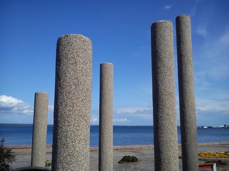 gray concrete pillars on the embankment of the lake, and in the background - blue sky and clouds