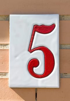 House number 5 over brick sunny wall. Houses with personality concept