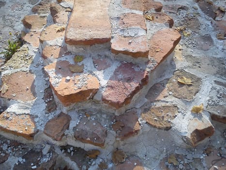 The restored wall of the building of Roman times. Sunlight accentuates the warm brown-red shades of uneven bricks. Archaeological excavations of steps and walls of ancient buildings.