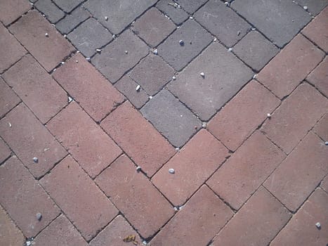 Burgundy and gray street paving tiles with small white pebbles. Rectangular decorative tile on the road. Rough edges of concrete. Tiles laid diagonally.