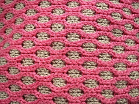 Close-up of decorative knitting. Machine or neat hand-knitted thing. The basis is beige yarn, the outer ornament is pink threads of the same thickness. Smooth hinges. Ovals or honeycombs as a pattern