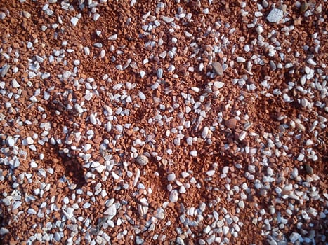 Fine decorative color granite crushed stone. Red-brown colored stone chips are used for landscaping. Crushed marble, granite, gravel or sand. Spots of fine white pebbles on heterogeneous soil.