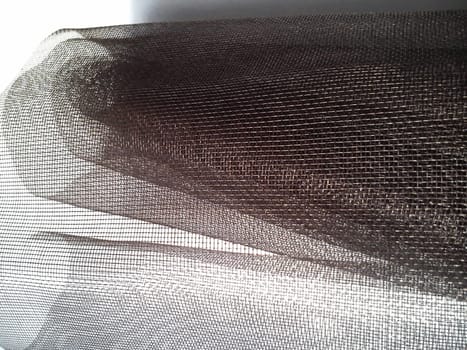 Mosquito net in a roll. Brown synthetic material on a white background. Weaving plastic threads. Convoluted lattice