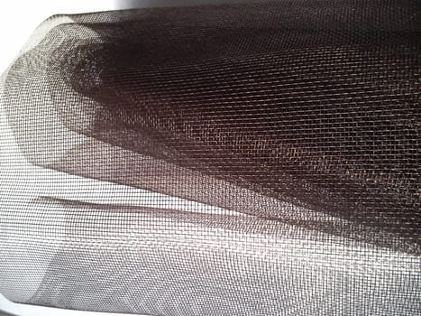 Mosquito net in a roll. Brown synthetic material on a white background. Weaving plastic threads. Convoluted lattice