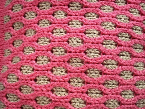 Close-up of decorative knitting. Machine or neat hand-knitted thing. The basis is beige yarn, the outer ornament is pink threads of the same thickness. Smooth hinges. Ovals or honeycombs as a pattern