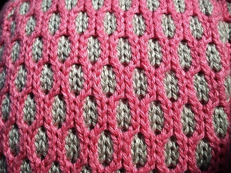 Close-up of decorative knitting. Machine or neat hand-knitted thing. The basis is beige yarn, the outer ornament is pink threads of the same thickness. Smooth hinges. Ovals or honeycombs as a pattern.