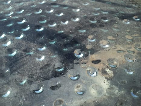Condensed water in the form of hanging drops, photographed from above. Drops gathered under a stack covering an ancient Roman excavation. Dust on the glass. Rays of the sun under glass