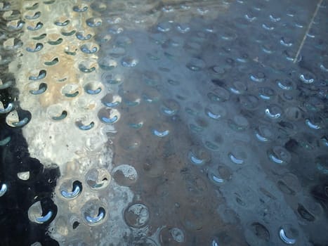 Condensed water in the form of hanging drops, photographed from above. Drops gathered under a stack covering an ancient Roman excavation. Dust on the glass. Rays of the sun under glass.
