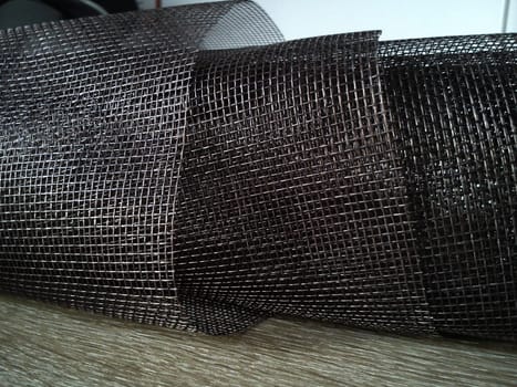 Mosquito net in a roll. Brown synthetic material on a white background. Weaving plastic threads. Convoluted lattice