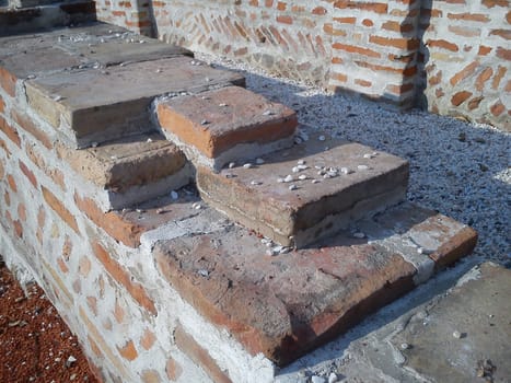 Old roman brick. The restored wall of the building of Roman times. Sunlight accentuates the warm brown-red shades of uneven bricks. Archaeological excavations of steps and walls of ancient buildings.