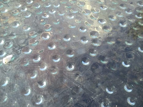 Condensed water in the form of hanging drops, photographed from above. Drops gathered under a stack covering an ancient Roman excavation. A little dust on the glass. Rays of the sun under glass.