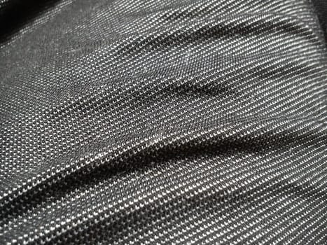 Textile fabric made on a loom by weaving mutually perpendicular yarns. Gray synthetic fabric for sewing clothes, upholstery and other products. Material close-up. Crumpled waves on the fabric.