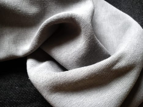 Close-up and texture of a knitted fabric or scarf of gray color, slightly folded round and wrinkled. A play of light and shadow in natural daylight. Soft, warm cotton or natural wool