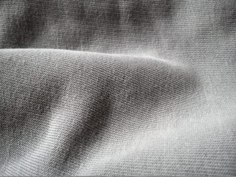 texture of a gray knitted fabric, slightly folded in waves or wrinkled. The play of light and shadow on a machine-knitted fabric in natural daylight. Soft, thick cotton material.