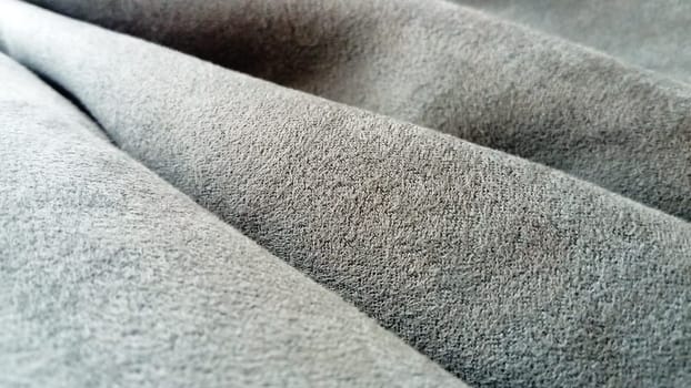 A close-up of velvety dense fabric for curtains of gray color, randomly folded by beautiful smooth waves. Natural daylight