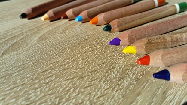 Multi-colored wooden pencils of a triangular shape in a section are intended for the development of fine motor skills of the child's hand. Pencils lie on a wooden table in natural light.