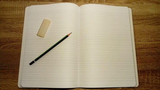 U-turn notebook with white blank sheets. On the left page are a graphic pencil and eraser. Soft light